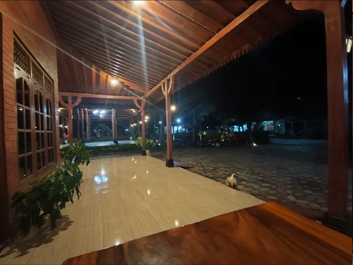 Teras kayu Rumah Joglo Alfarobi dengan pencahayaan malam yang hangat.